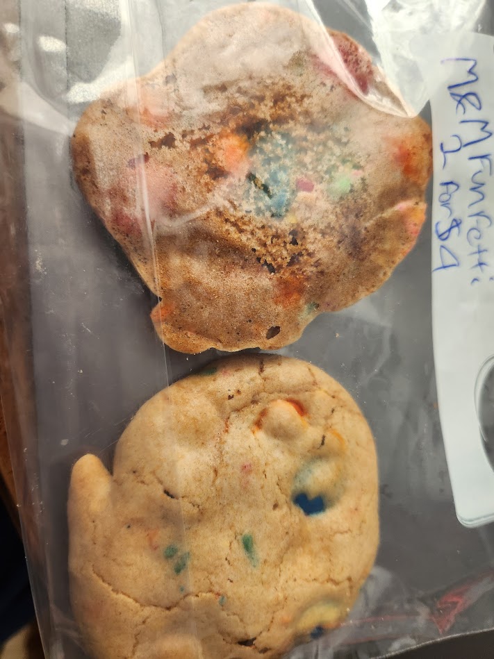 An image of two confetti cookies sprinkled with M&Ms in a plastic bag.